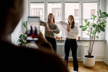 Teenage girl with mobile phone filming female friends dancing against in living room - MASF18672