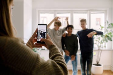 Teenager-Mädchen mit Mobiltelefon filmt männliche Freunde beim Tanzen im Wohnzimmer - MASF18675