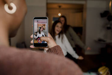 Mädchen mit Smartphone beim Filmen von tanzenden Freunden im Wohnzimmer zu Hause - MASF18676