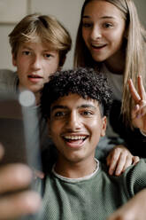 Lächelnder Teenager, der zu Hause ein Selfie mit Freunden über sein Mobiltelefon macht - MASF18680