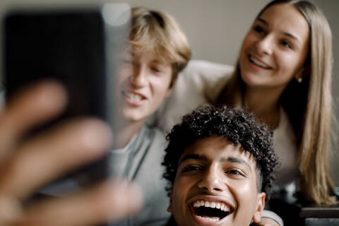 Fröhliche männliche und weibliche Freunde im Teenageralter, die zu Hause ein Selfie mit ihrem Mobiltelefon machen, lizenzfreies Stockfoto