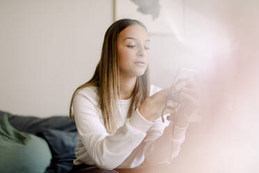 Teenager-Mädchen nutzt soziale Medien auf dem Smartphone, während sie zu Hause sitzt - MASF18684