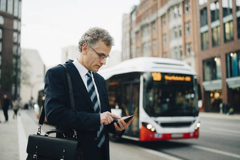 Älterer Geschäftsmann, der sein Smartphone benutzt, während er in der Stadt steht - MASF18700