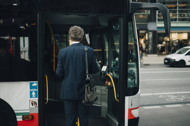 Rückansicht eines männlichen Unternehmers, der während einer Geschäftsreise in der Stadt in einen Bus einsteigt - MASF18701