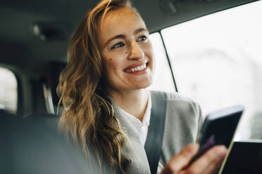 Confident smiling entrepreneur looking away while sitting in taxi - MASF18713