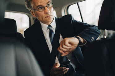 Businessman wearing wristwatch during business trip while sitting in taxi - MASF18719