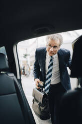 Reifer männlicher Unternehmer, der während einer Geschäftsreise in ein Taxi steigt - MASF18722