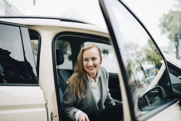 Lächelnde Unternehmerin beim Aussteigen aus einem Taxi während einer Geschäftsreise - MASF18723