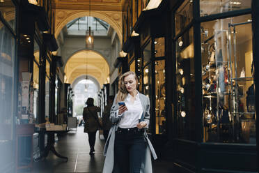 Nachdenkliche Geschäftsfrau, die ein Smartphone benutzt, während sie in der Stadt steht - MASF18735