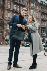 Businessman and businesswoman using phone while standing in city - MASF18754