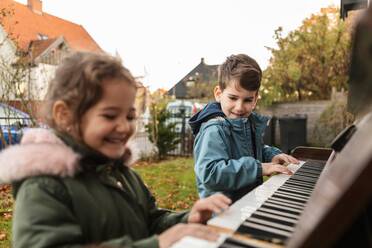 Lächelndes Mädchen spielt mit seinem Bruder im Hinterhof Klavier - MASF18833