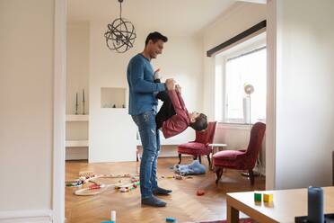 Smiling father lifting playful son while standing in living room - MASF18839