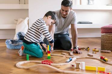 Lächelnder Vater spielt mit seinem Sohn, während er im Wohnzimmer kniet - MASF18853