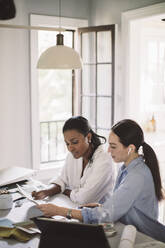 Side view of architect discussing with coworker while working at table in home office - MASF18862