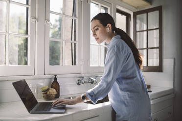 Side view of female professional using laptop on counter at home office - MASF18879