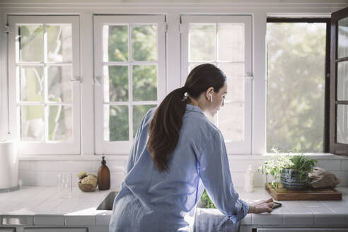 Rückansicht einer Geschäftsfrau, die ihr Smartphone auf der Küchentheke im Büro zu Hause benutzt - MASF18880
