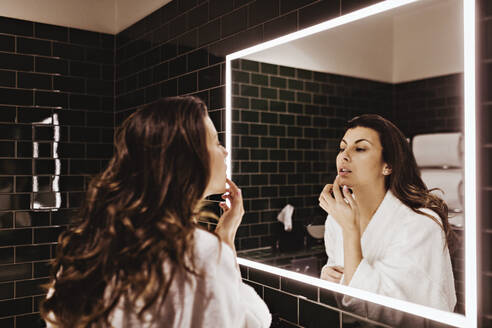 Mittlere erwachsene Frau schaut in den Spiegel und trägt Lippenbalsam auf - MASF18896