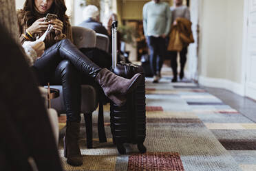 Niedriger Ausschnitt einer mittleren erwachsenen Frau, die ein Mobiltelefon benutzt, während sie auf einem Stuhl in einer Hotellobby sitzt - MASF18910