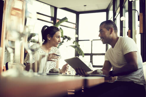 Niedriger Blickwinkel von Mann und Frau mit digitalem Tablet im Gespräch, während sie am Tisch in einem Café sitzen - MASF18930
