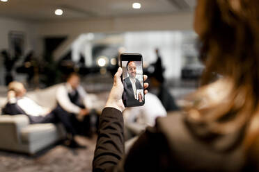 Weibliche Führungskraft bespricht sich per Videokonferenz mit einem männlichen Fachmann auf einem Smartphone im Büro - MASF18947