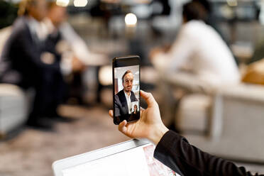 Männliche und weibliche Kollegen unterhalten sich per Videokonferenz auf einem Smartphone im Büro - MASF18949