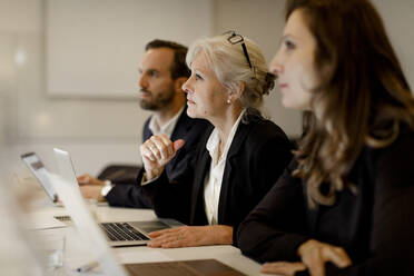 Reife Geschäftsfrau sitzt mit Kollegen am Konferenztisch in einer Bürobesprechung - MASF18951