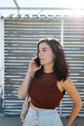 Schöne Frau, die ein Smartphone benutzt, während sie an einem sonnigen Tag vor einem Fensterladen steht - JMPF00137