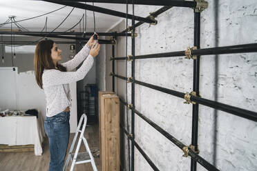 Mid adult woman on step ladder hanging lightbulb in her new shop - CUF55605