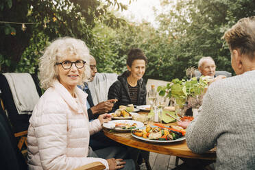 Porträt einer lächelnden älteren Frau, die mit Freunden am Esstisch sitzt, während einer Dinnerparty - MASF18986
