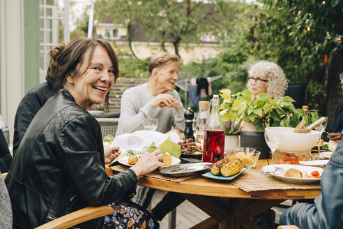 Porträt einer lächelnden älteren Frau, die mit männlichen und weiblichen Freunden am Esstisch sitzt und eine Dinnerparty genießt - MASF19001