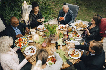 High angle view of senior male and female friends enjoying dinner at dining table during back yard garden party - MASF19002