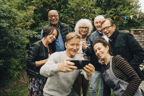 Smiling senior man taking selfie with female and male friends during garden party at back yard stock photo