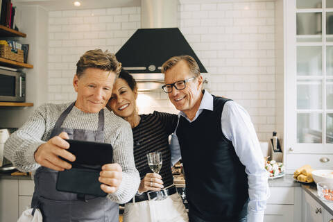 Smiling man taking selfie with friends standing in kitchen at home stock photo