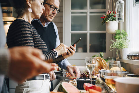 Senior woman showing smart phone to man while preparing dinner in kitchen stock photo