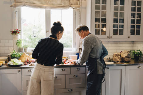 Active female and male senior friends cutting watermelon at counter in kitchen stock photo