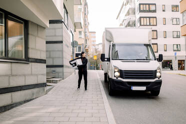 Junge Zustellerin mit Paket auf dem Fußweg in der Stadt - MASF19057