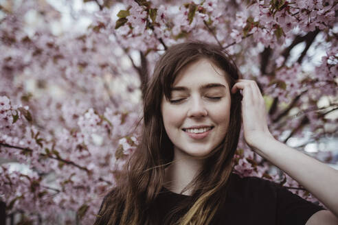 Smiling woman with eyes closed standing against tree - MASF19067