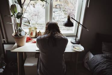 Rear view of worried woman sitting against window - MASF19069