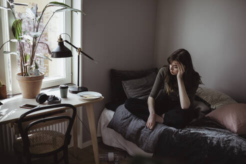 Depressed woman sitting on bed at home - MASF19078