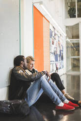 Young man sitting with male friend in corridor of university - MASF19110