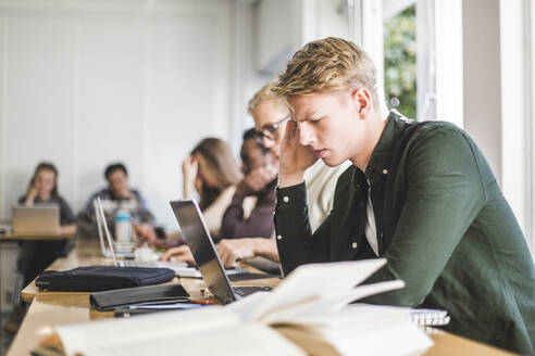 Entschlossener junger Mann benutzt Laptop im Klassenzimmer - MASF19139