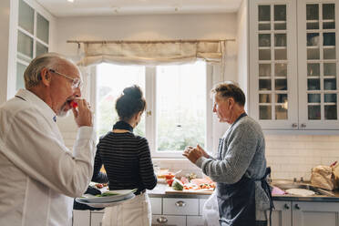 Man eating watermelon while friends talking in kitchen - MASF19154