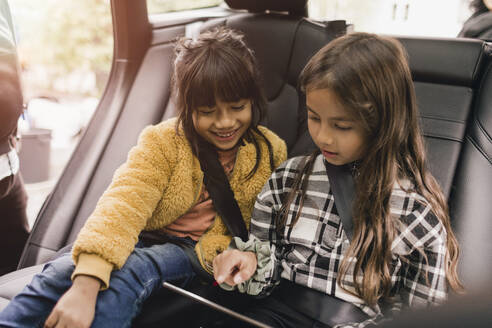 Schwestern, die im Elektroauto sitzend ein digitales Tablet benutzen - MASF19176