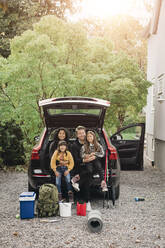 Smiling parents sitting with daughters in trunk of electric car - MASF19179