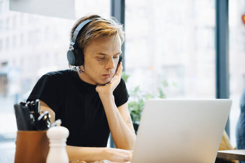 Confident young transgender sitting while using laptop in bright cafe - MASF19197