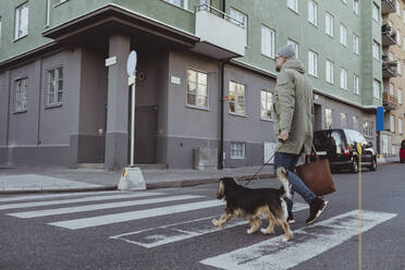 Mann in voller Länge beim Überqueren der Straße mit Hund in der Stadt - MASF19251