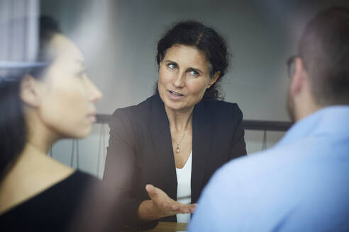 Confident mature female financial advisor discussing with businessman and businesswoman during meeting at office - MASF19306