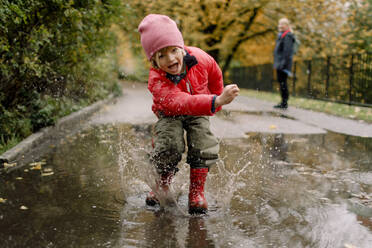 Playful boy splashing water in puddle on road - MASF19314