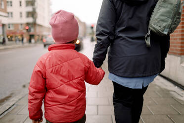 Rear view of grandson holding hand of grandmother while walking on footpath in city - MASF19320