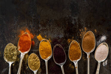 High angle close up of variety of spices on silver spoons. - ISF24235